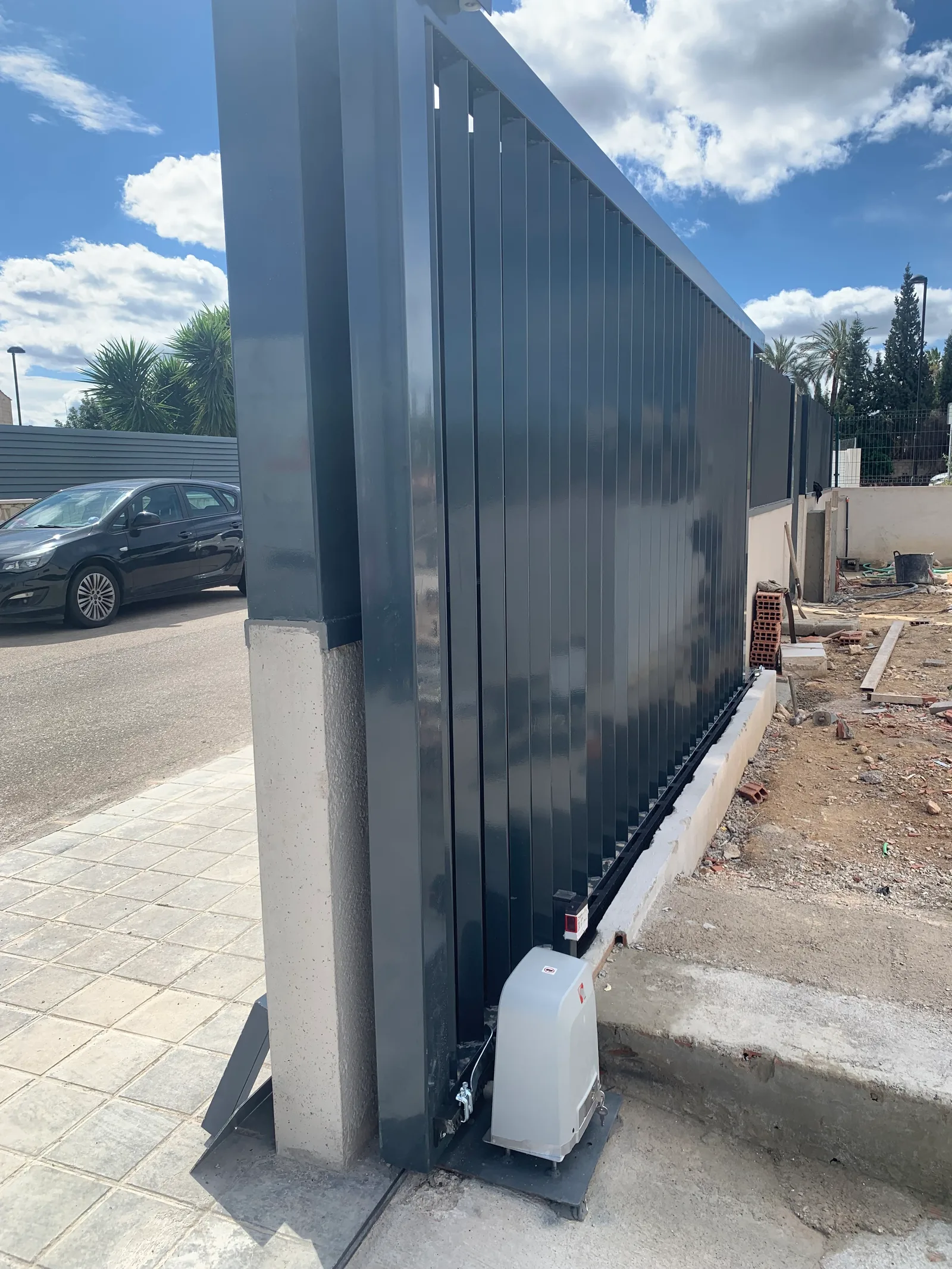 Puerta corredera gris instalada con motor en un acceso